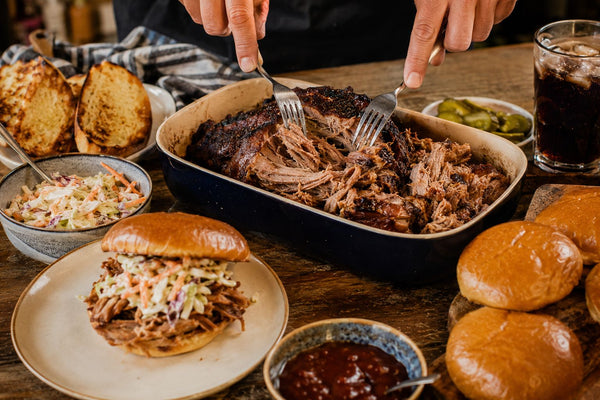 Pulled pork som dras isär med gafflar, bröd och coleslaw bredvid